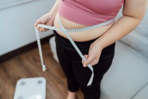 Close up of a woman measuring around her midsection, wanting to lose weight and in need of semaglutide treatment.