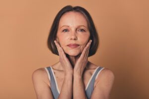 Older woman touching her face, happy with her combined cosmetic treatment results.