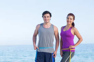 Two adults measuring their waists while comparing medical weight loss medication options